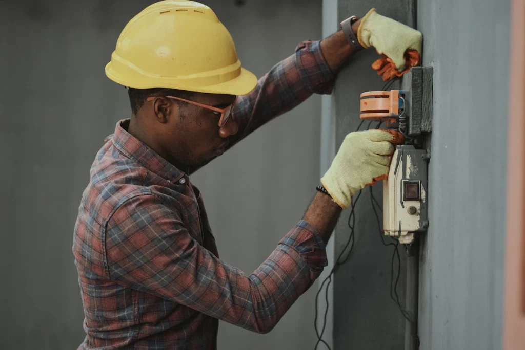 Technician in a hard hat and protective glasses inspecting wall-mounted equipment